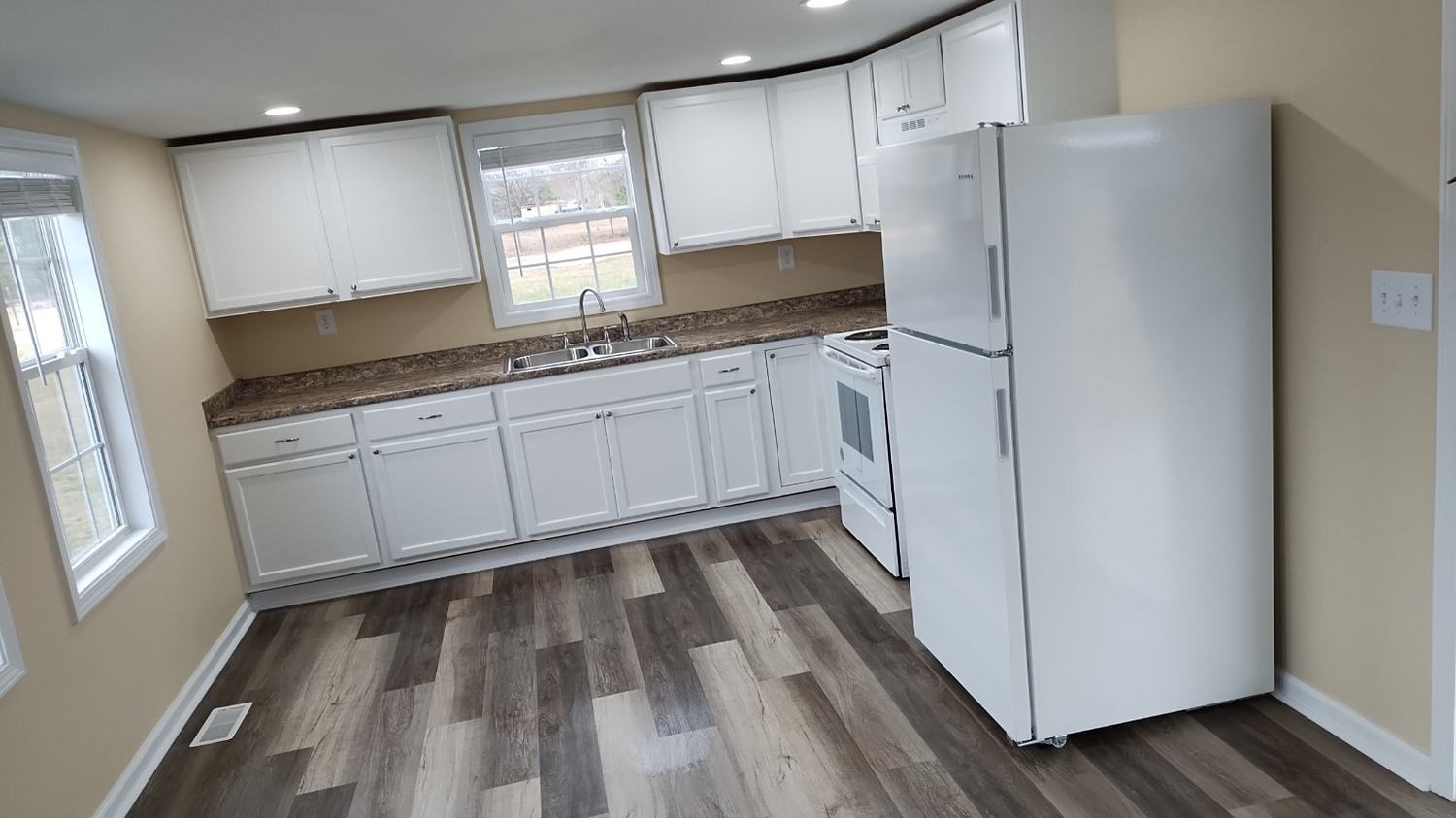 Completed kitchen with white cabinets, sink, countertop, trim, and plank flooring.