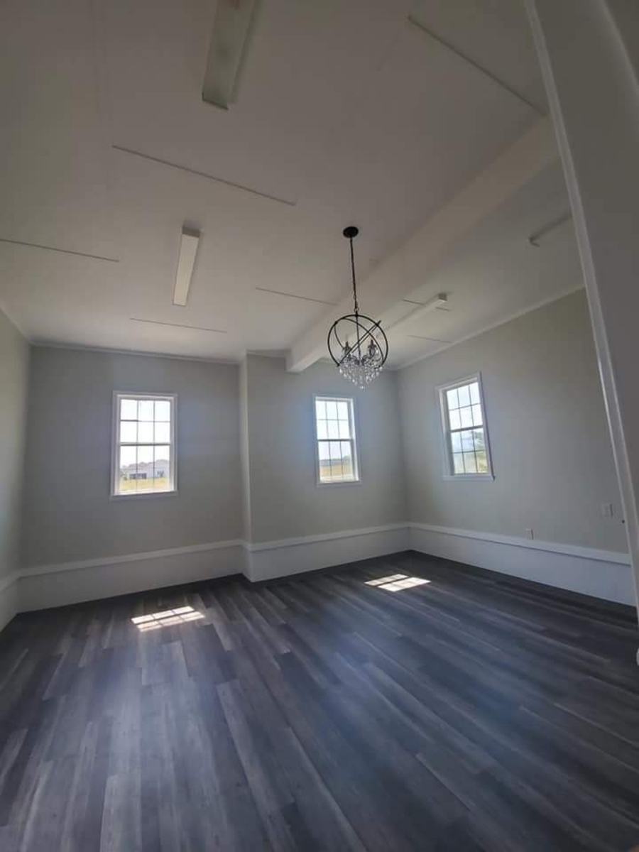 Completed open room with dark flooring, light walls, white trim, windows, ceiling detail, and hanging fixture.