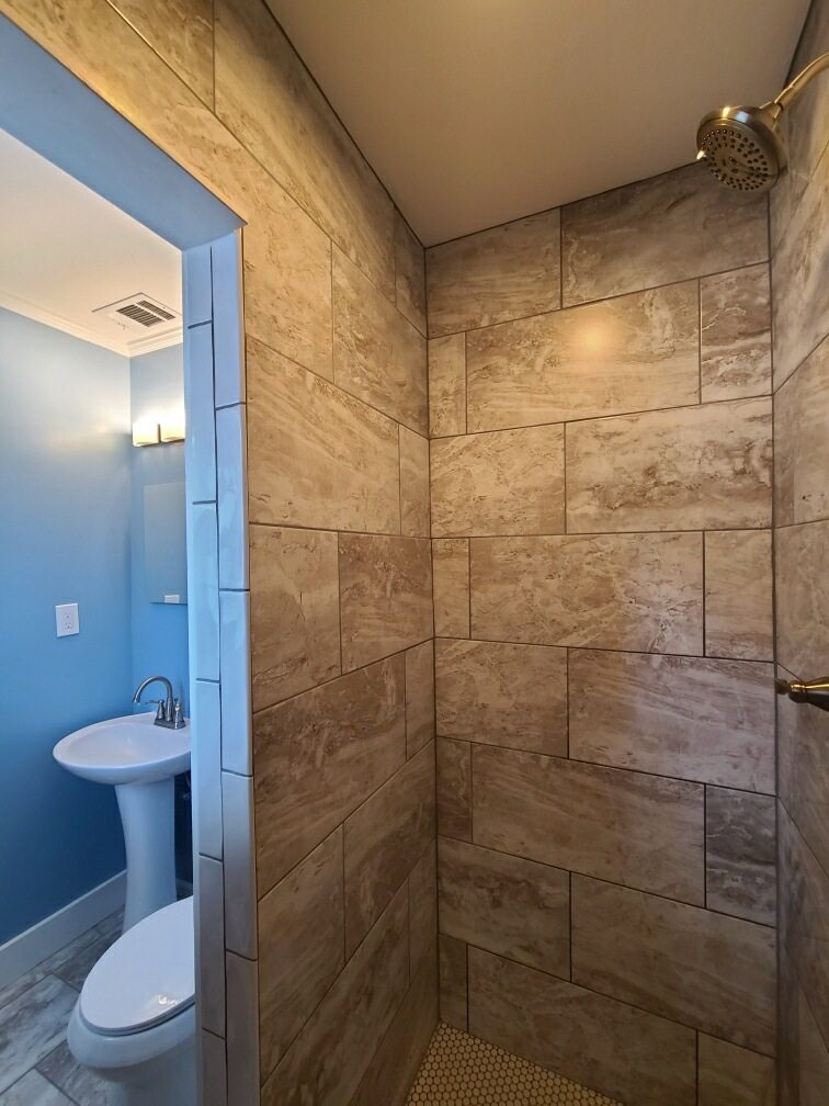 Travertine-tile walk-in shower with blue accent wall by MMAC Renovation