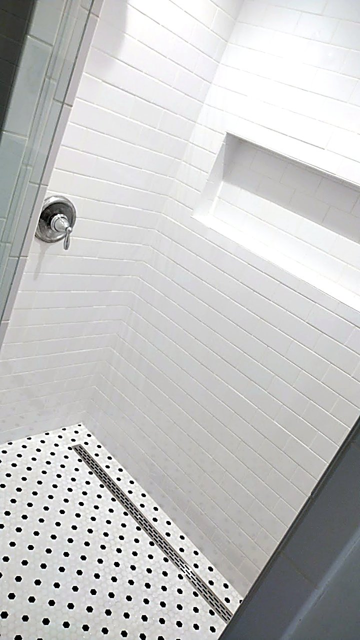 White subway-tile shower with penny-tile floor by MMAC Renovation