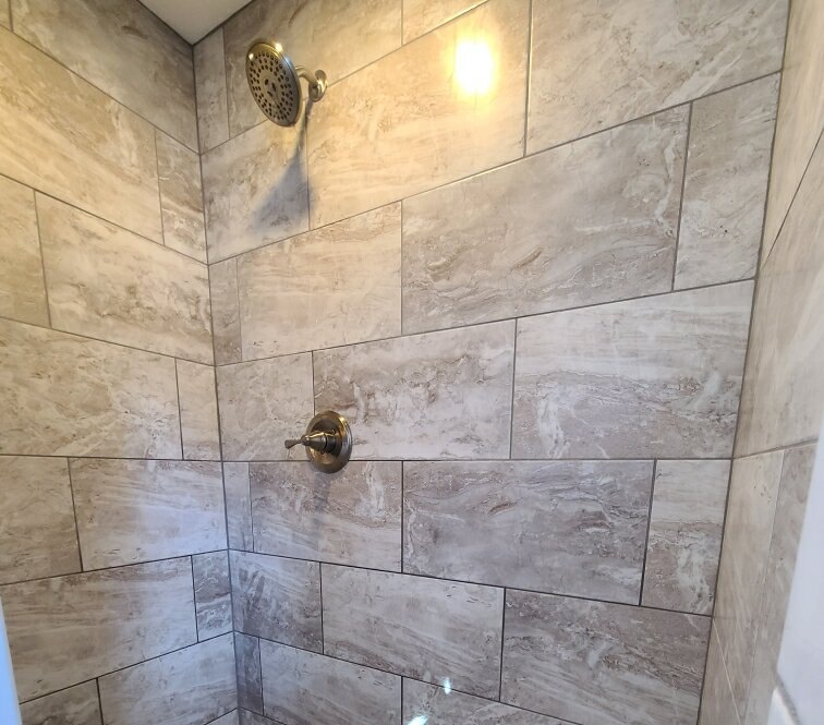 Travertine-tile shower with niche and fixtures by MMAC Renovation