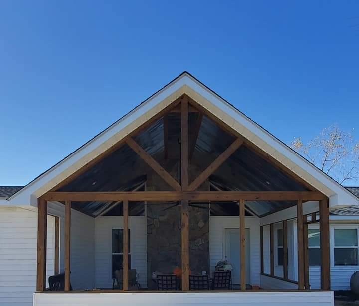 Covered porch addition with vaulted cedar timber trusses and stone column by MMAC Renovation