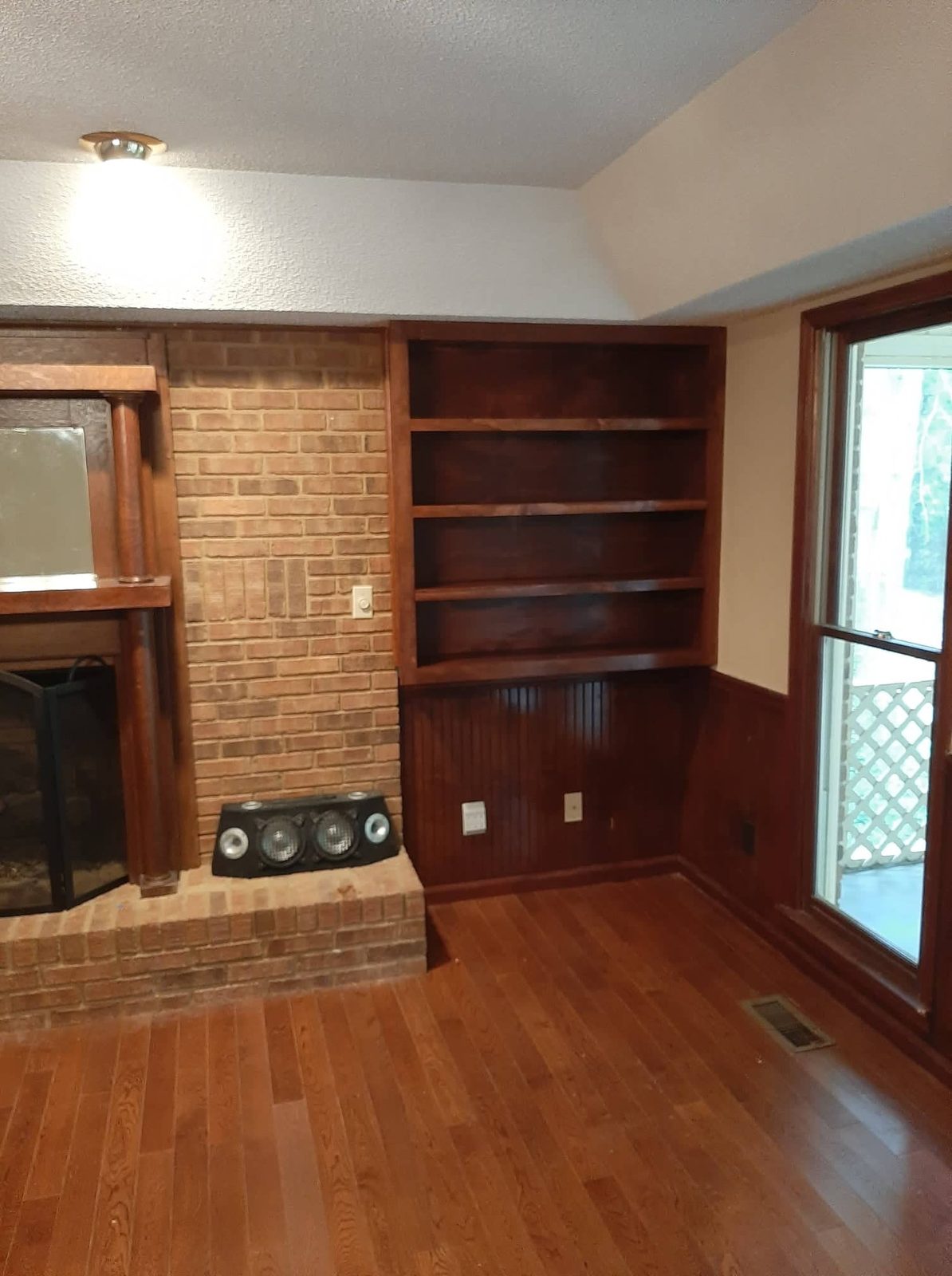 Brick fireplace flanked by custom built-in shelving with wood floor and wainscot