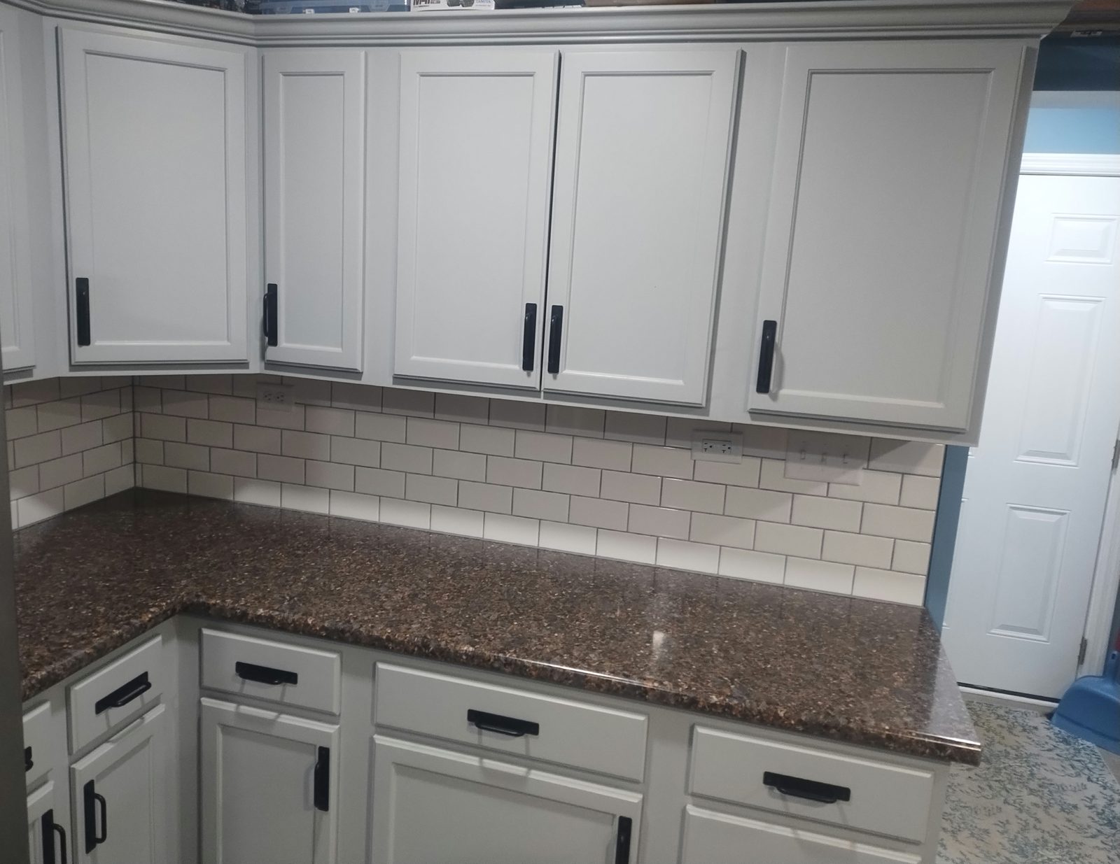 White kitchen cabinets with granite counters and subway-tile backsplash, completed by MMAC Renovation