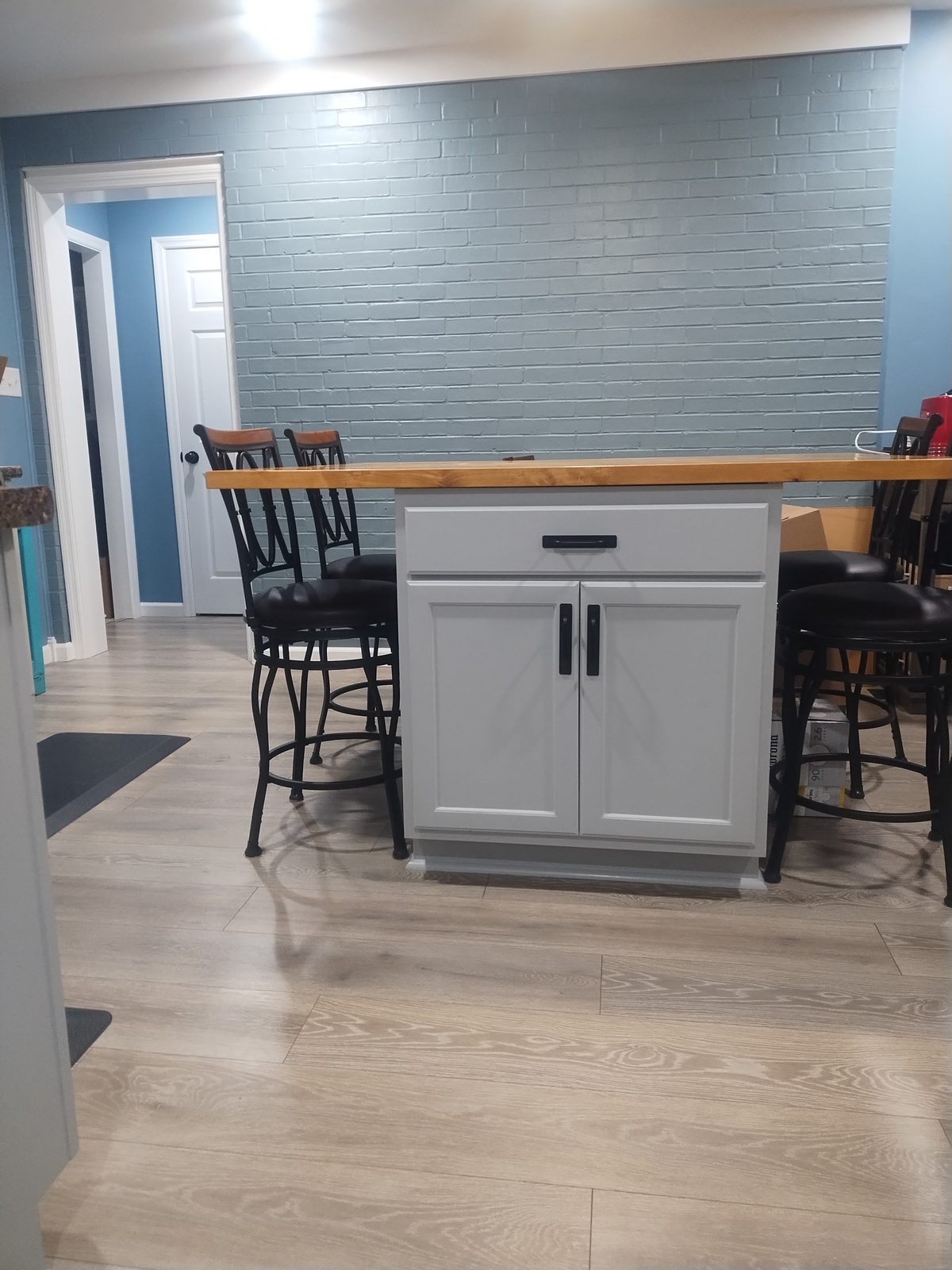 Kitchen island with bar stools, blue accent wall and plank flooring by MMAC Renovation